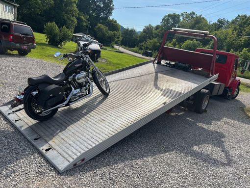 Motorcycle on a flatbed tow truck, parked on gravel driveway, sunny day.