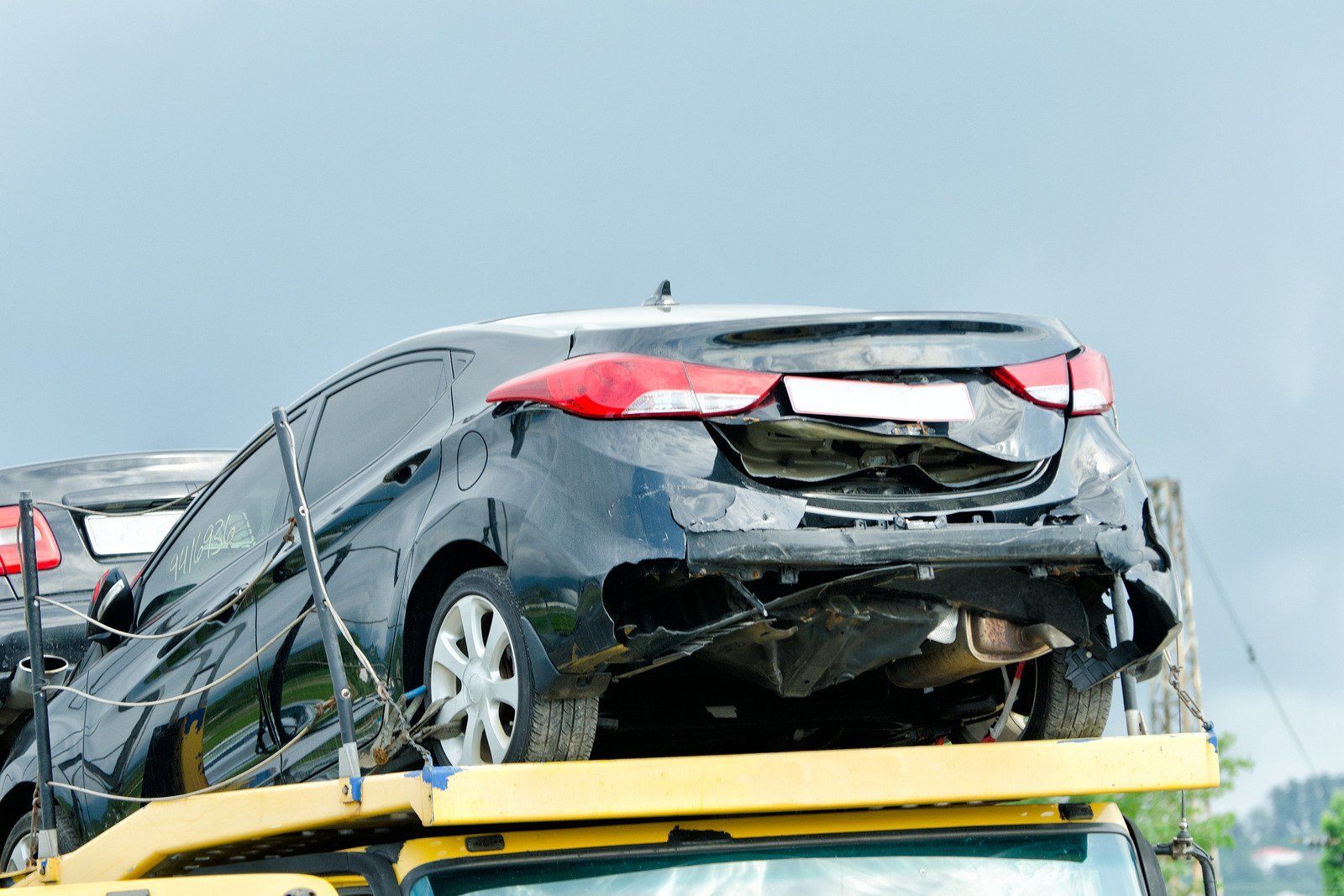 Black car with significant rear damage on a tow truck, likely headed for a junkyard.