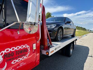 Red tow truck with a black sedan on its flatbed on a sunny day.