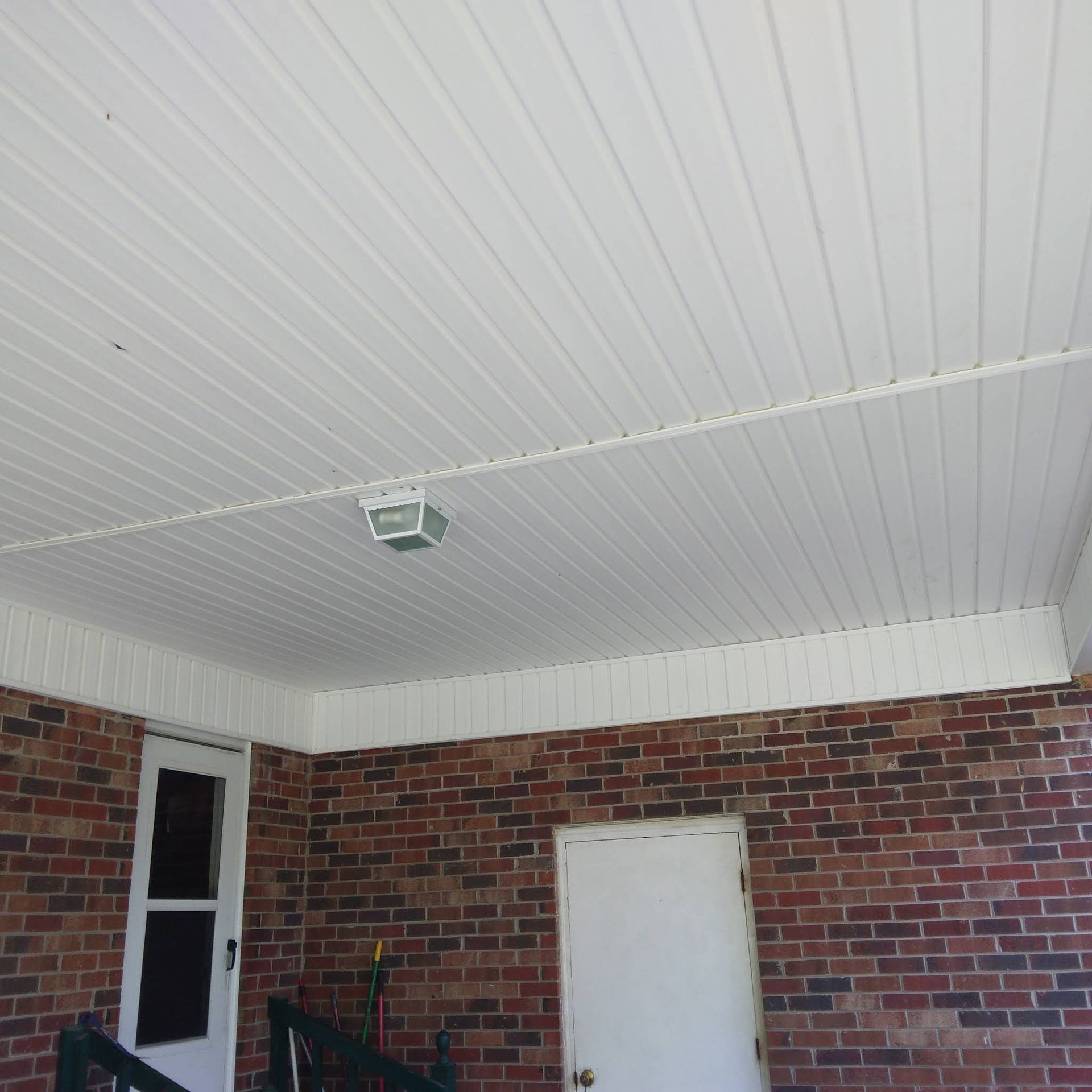 A porch with a white ceiling and a brick wall