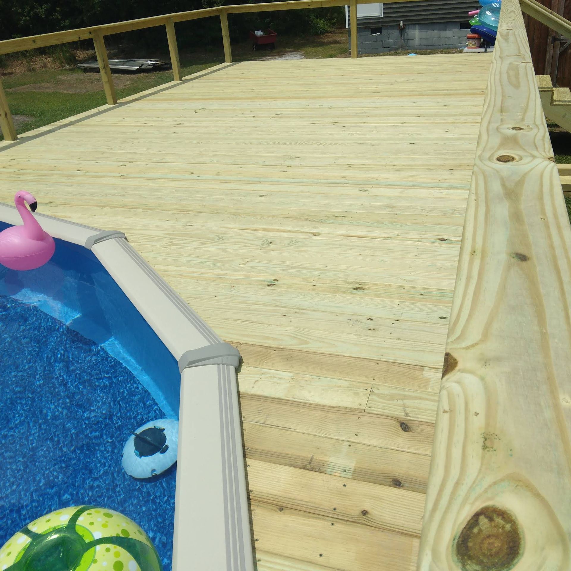 A wooden deck over a swimming pool with a pink flamingo float