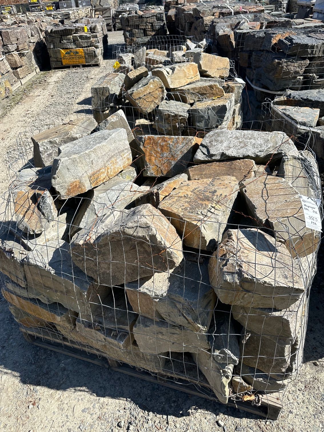 A pallet of large, rough-hewn gray and brown landscaping rocks, bound in wire mesh.