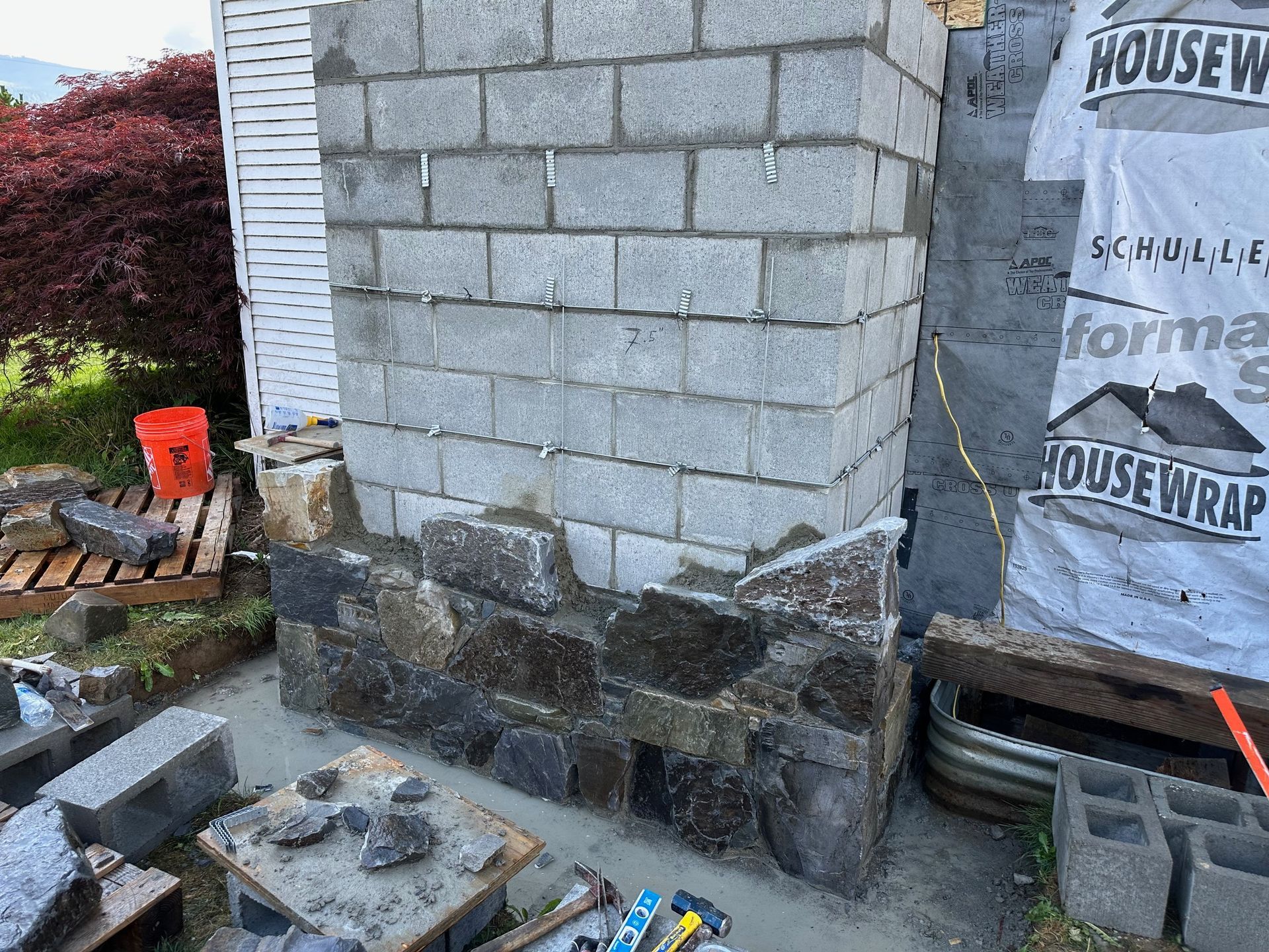 Stone and cinder block chimney under construction. Grey, brown stones and blocks are visible.