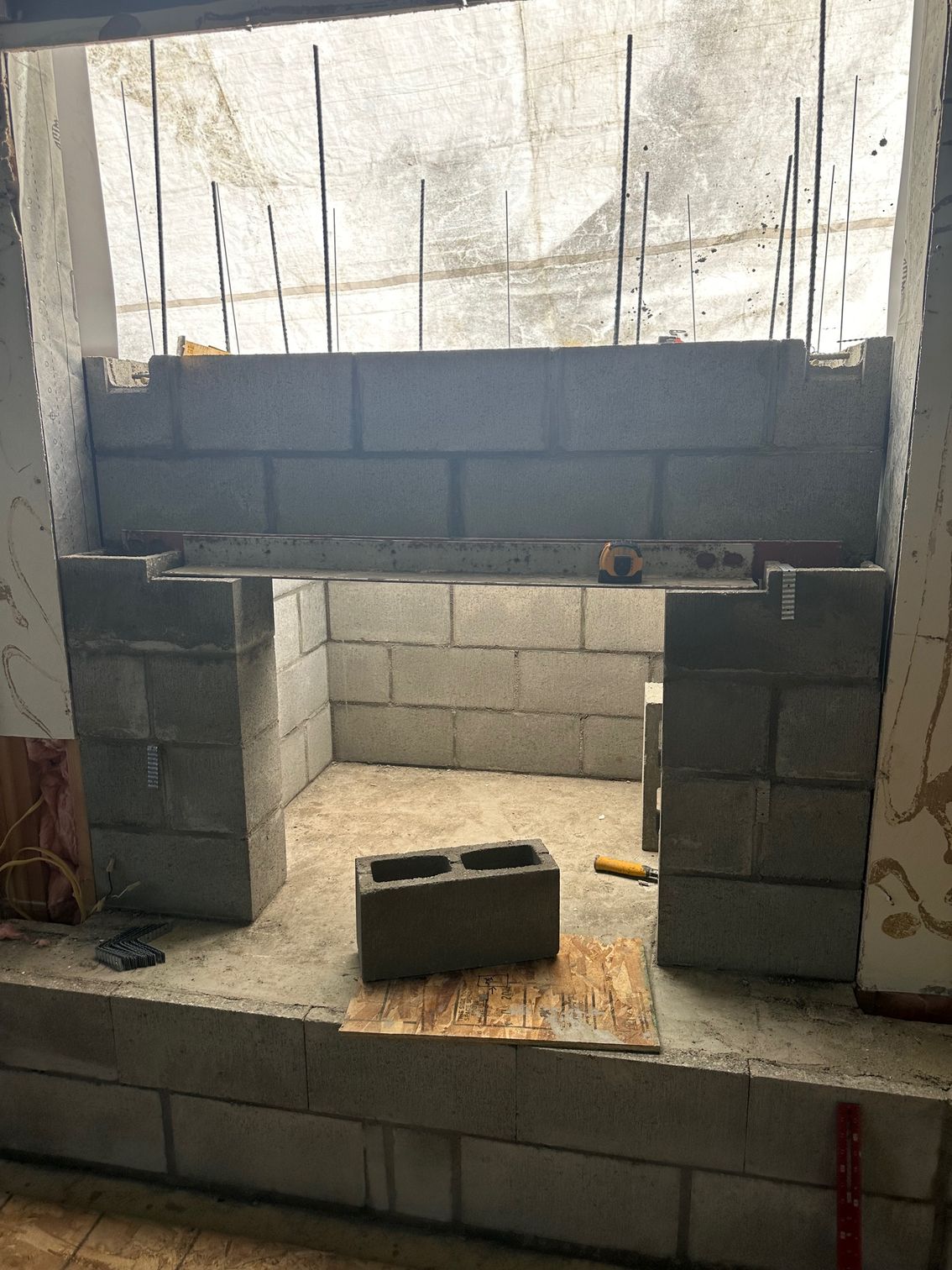Construction of a fireplace; gray concrete blocks are being laid, with metal rebar supports.