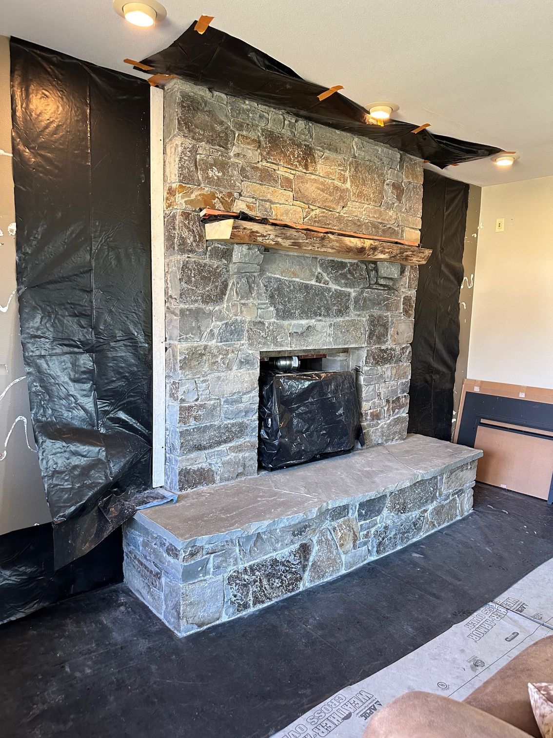 Stone fireplace under construction, covered in black protective sheeting.