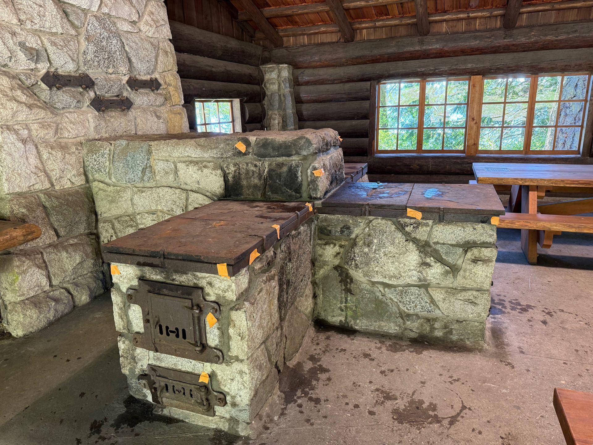 Stone fireplace and cooking area inside a rustic cabin, with wooden beams and a window.
