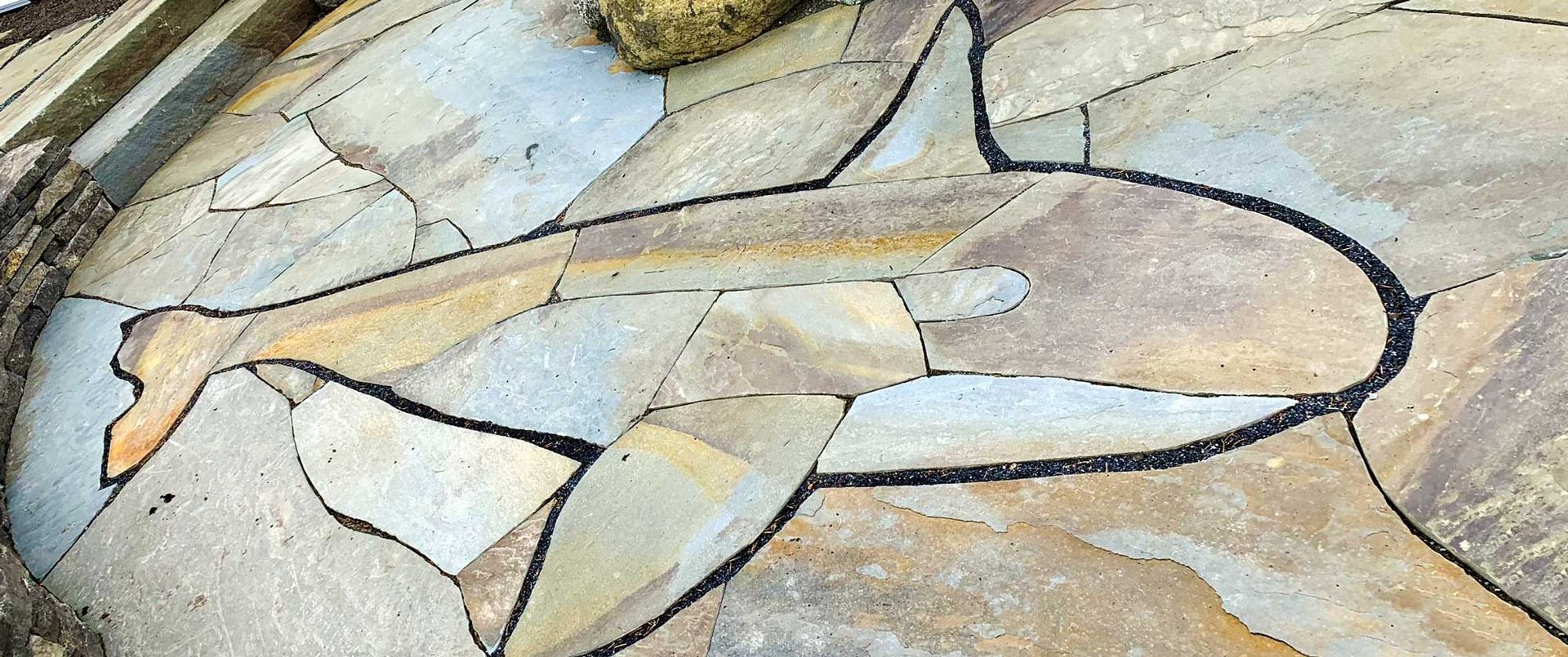 Mosaic of a shark on a stone surface with tan, gray, and black colors.