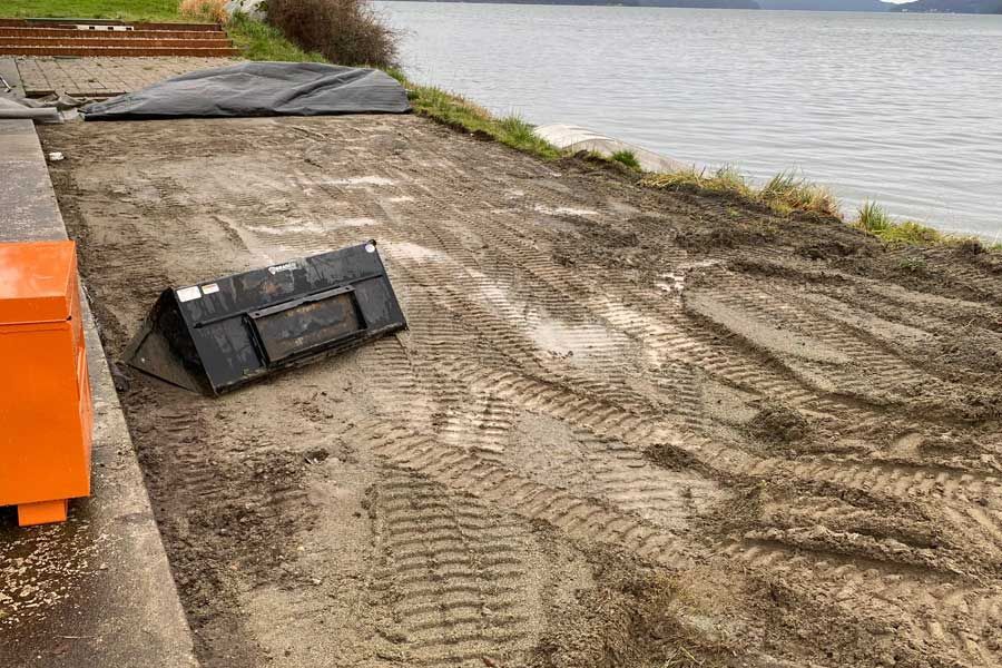 Muddy waterfront area with tire tracks, black bin, and orange structure.