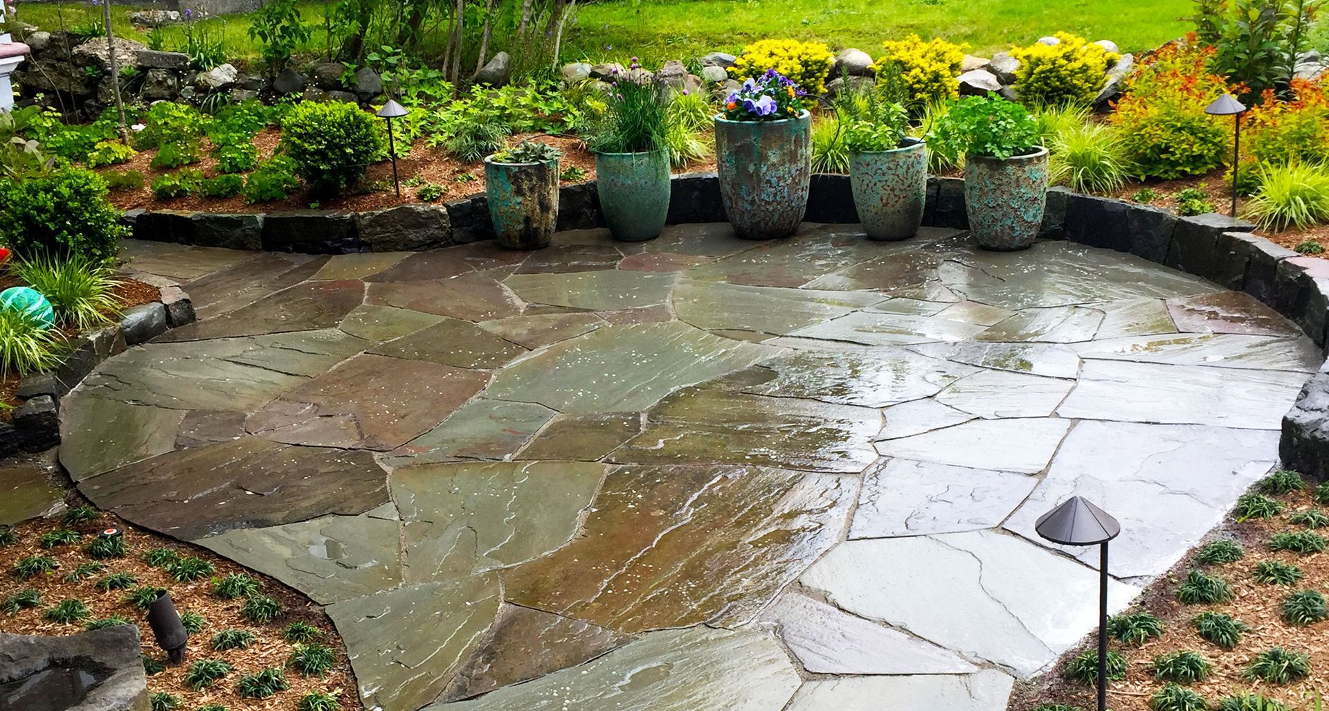 Stone patio with potted plants, surrounded by garden beds.