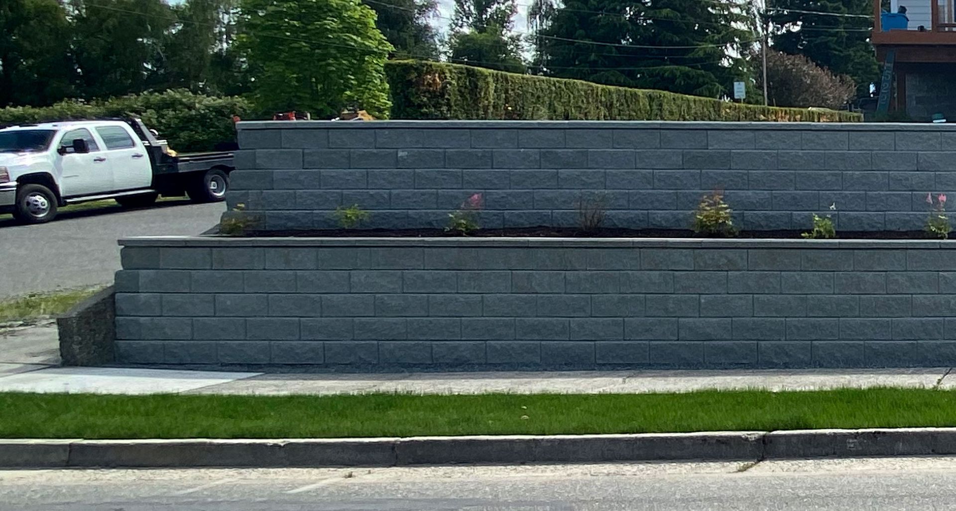 Gray tiered retaining wall with small pink flowers and a white truck on the left.