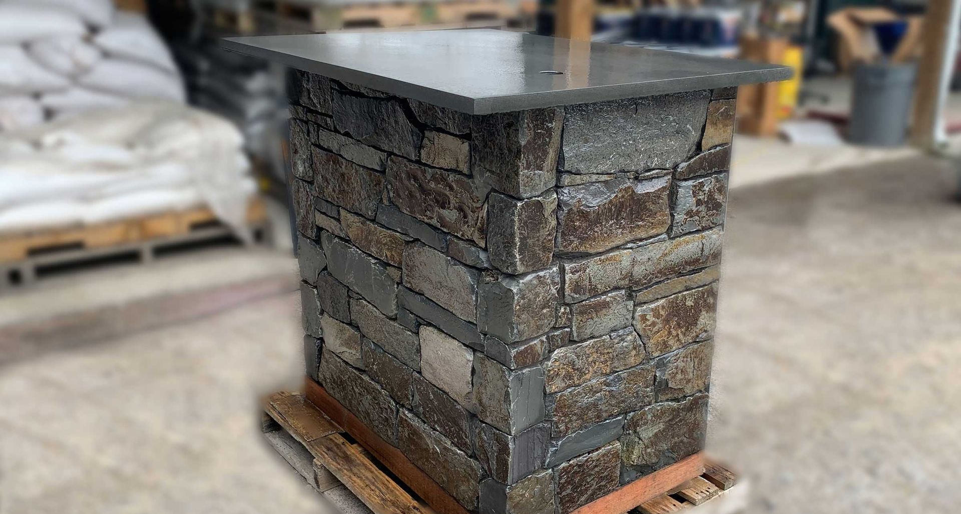 Stone pedestal with a dark countertop, sitting on a wooden pallet.