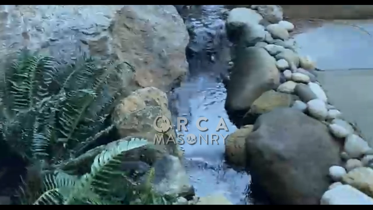 Waterfall feature with rocks, foliage, and flowing water.