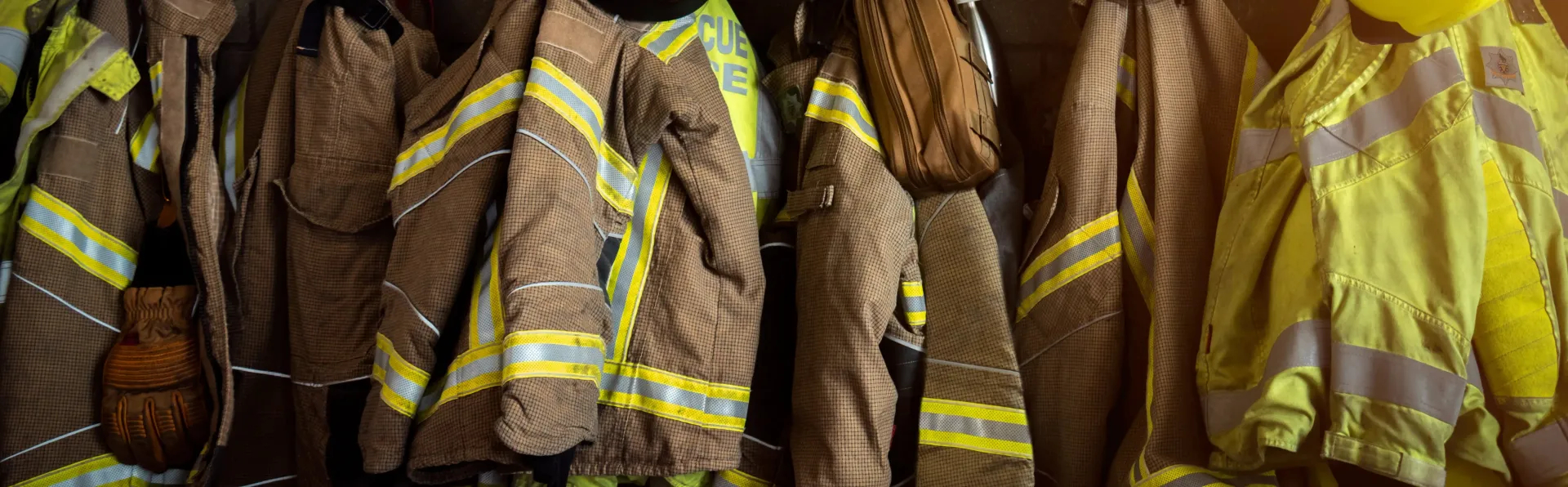 A row of firefighter jackets hanging on a rack.