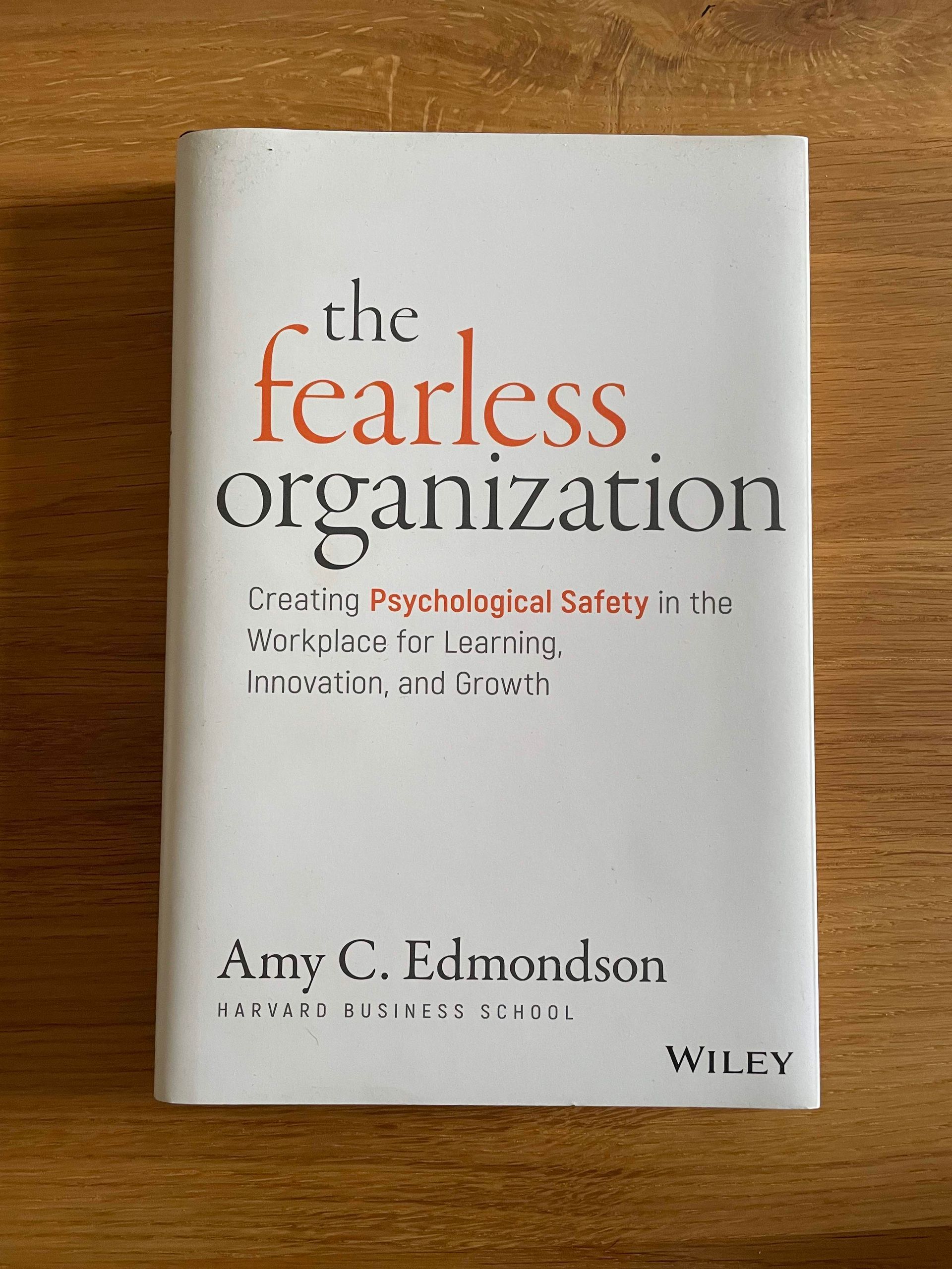 Picture of the book cover of the fearless organization by Amy C. Edmondson on a wooden surface. The book cover is white with black and orange font. The subtitle is: creating psychological safety in the workplace for learning, innovation, and growth.