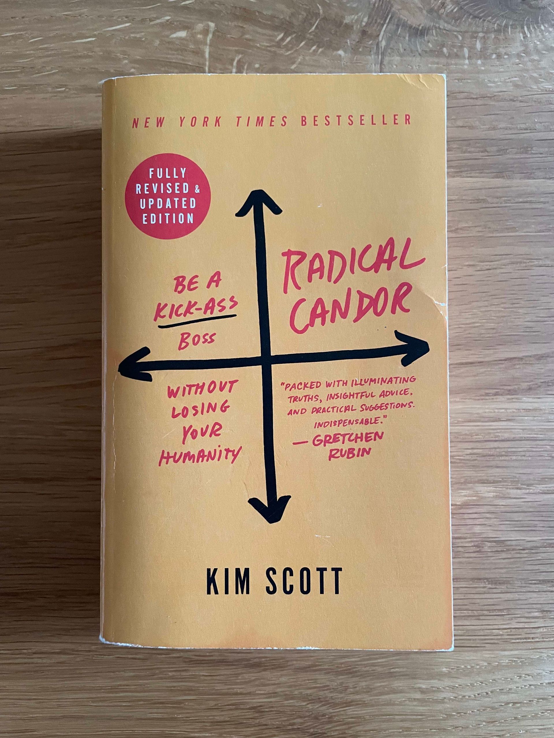 Picture of the book cover of radical candor by Kim Scott on a wooden surface. The book cover is yellow with black and red font. The subtitle is: be a kick-ass boss without losing your humanity.