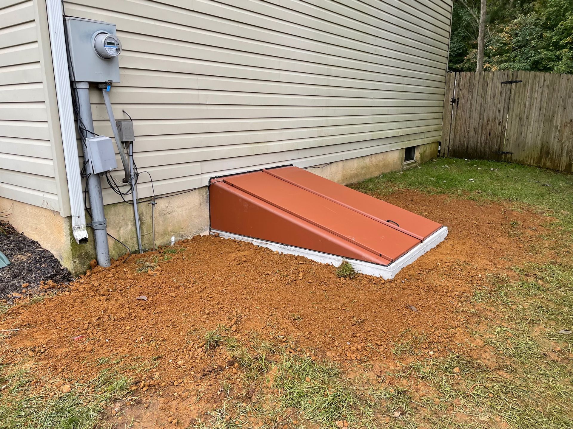 Brown basement door with tan siding, next to electrical panel on side of house.