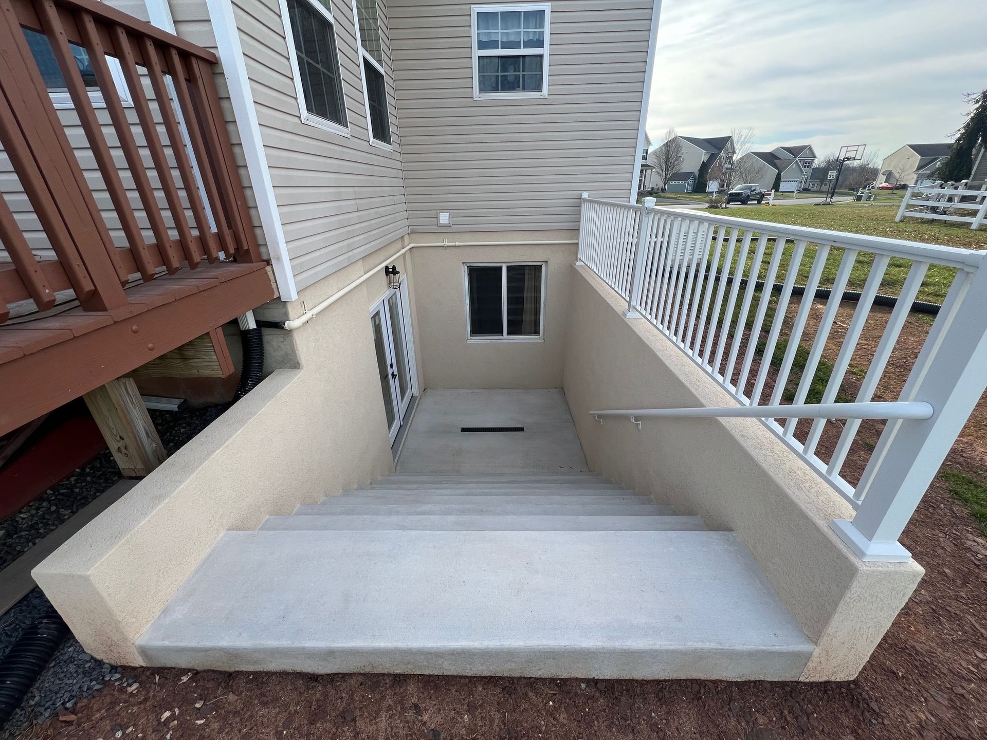 Staircase leading to a basement door, with railing on the right. Beige stucco walls and siding.