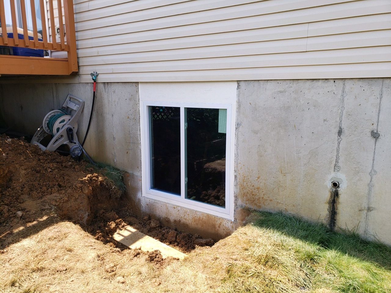A window is being installed in the basement of a house.