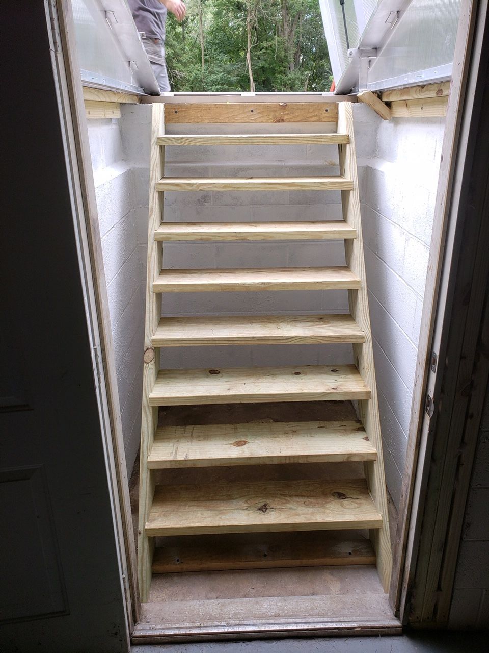 A man is standing on top of a wooden staircase in a basement.