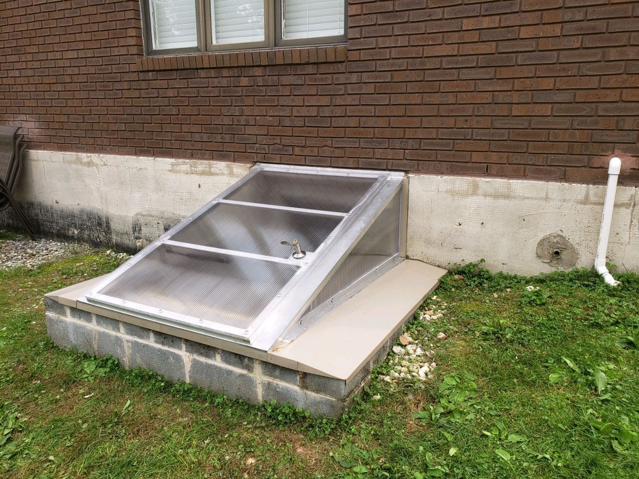 A brick wall with a window well in front of it.