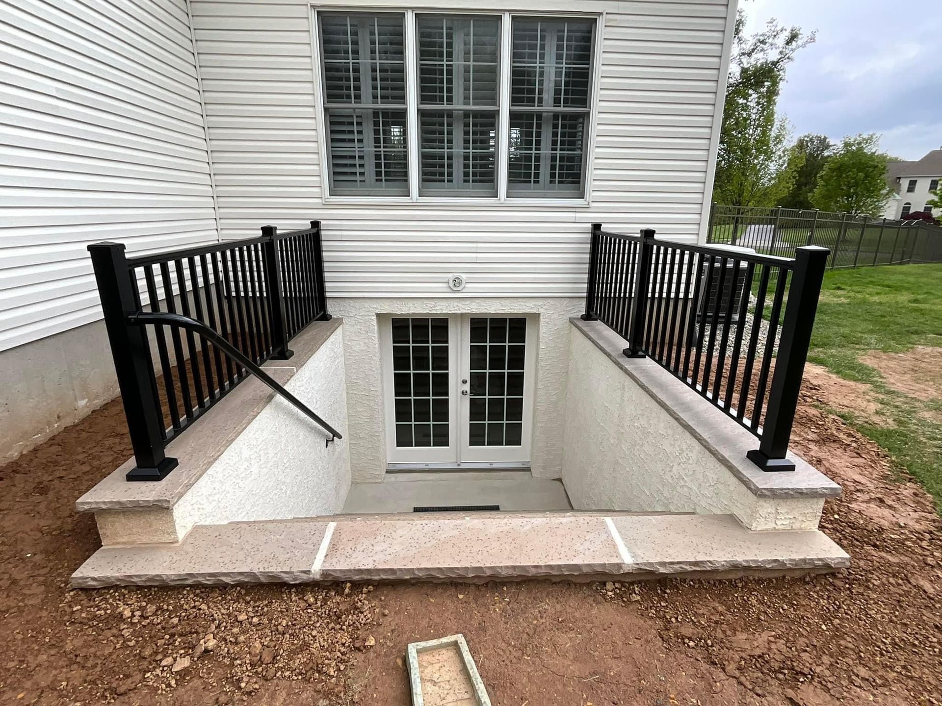 Exterior basement entrance with black railings, white double doors, and white siding.