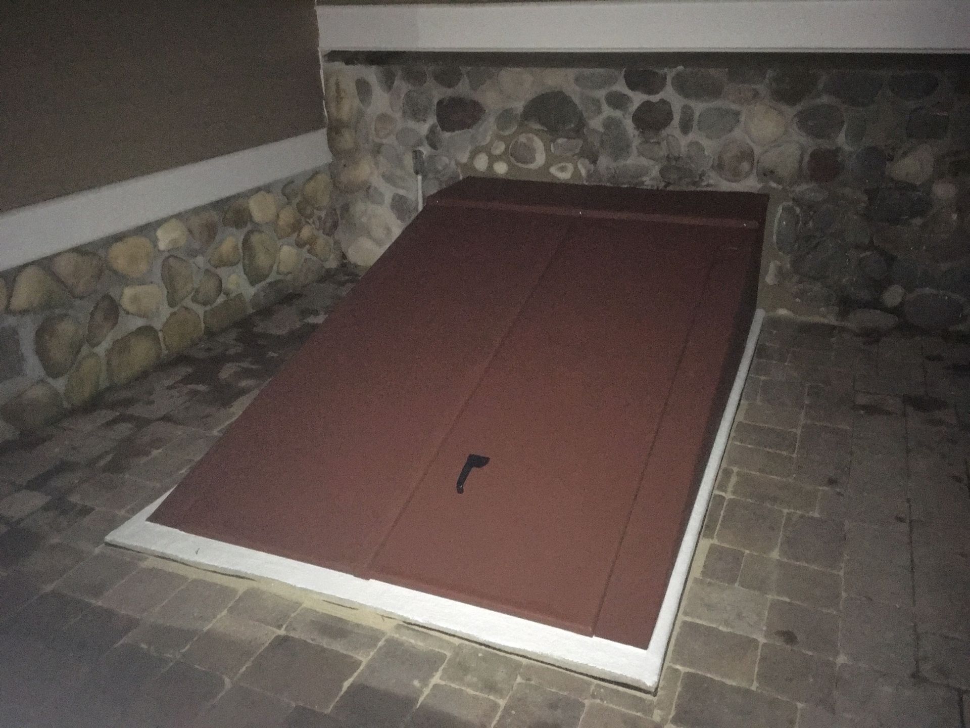 A red garage door is sitting on a brick floor in front of a stone wall.