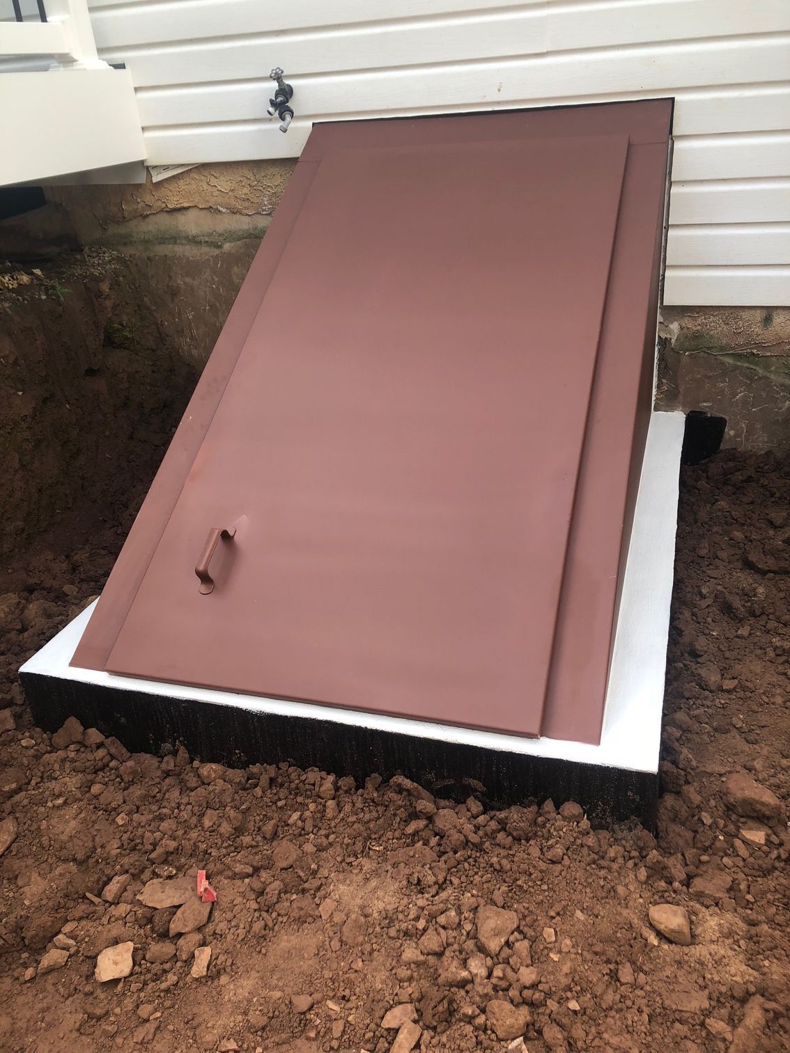 A brown door is sitting in the dirt next to a house.