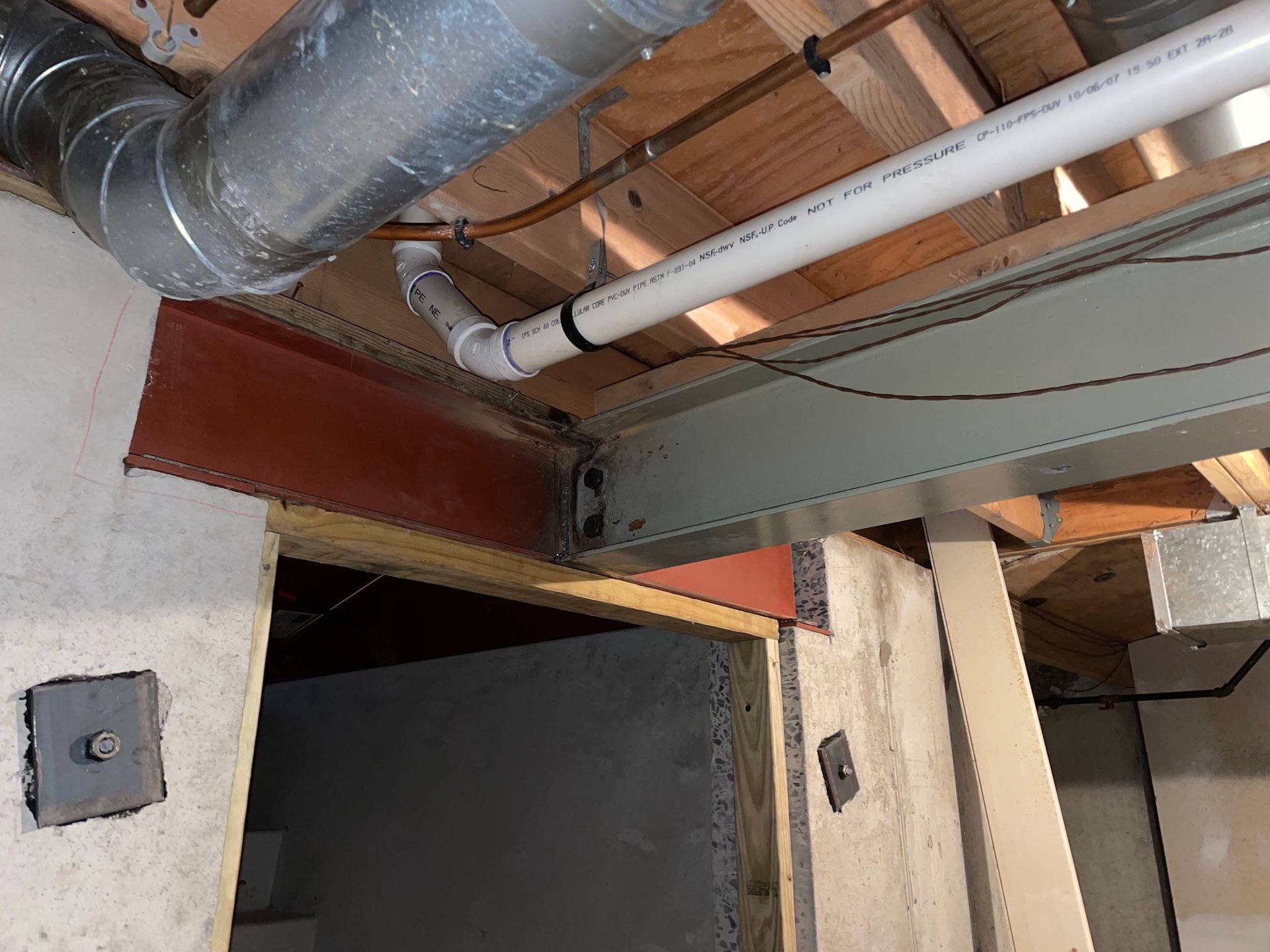 Basement ceiling view: metal beams, ductwork, plumbing, and concrete support structures are visible.