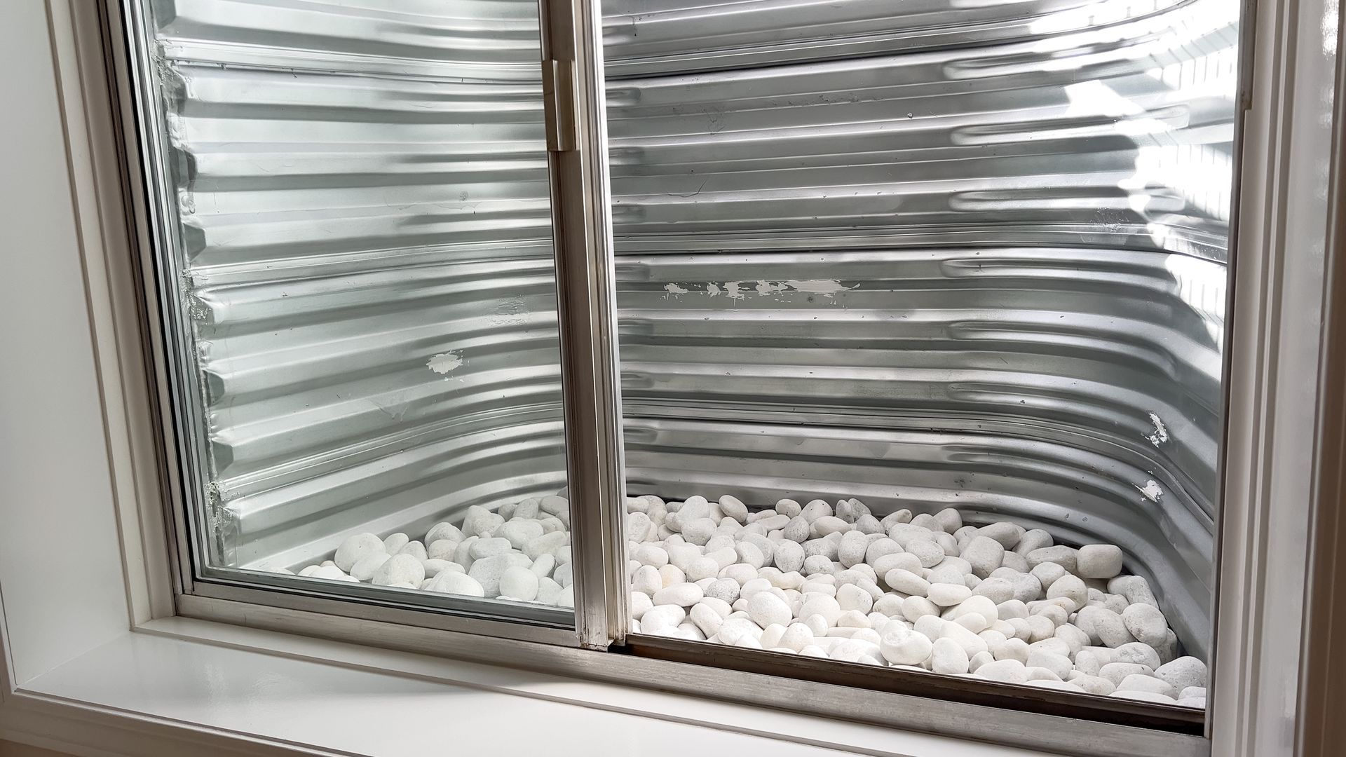 Window well filled with white rocks, visible through a window in a white frame.