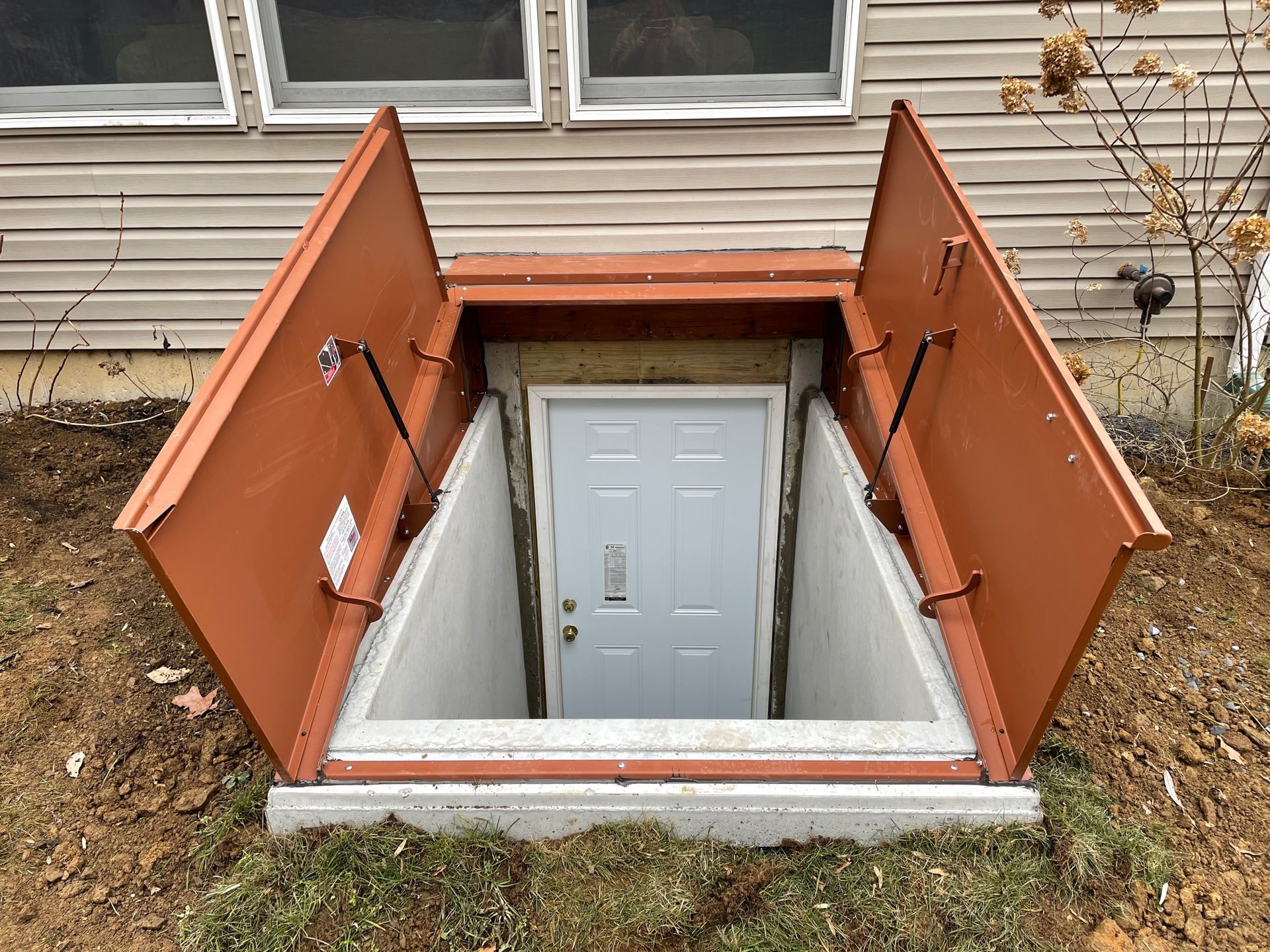 A basement door with a red cover is open in front of a house.