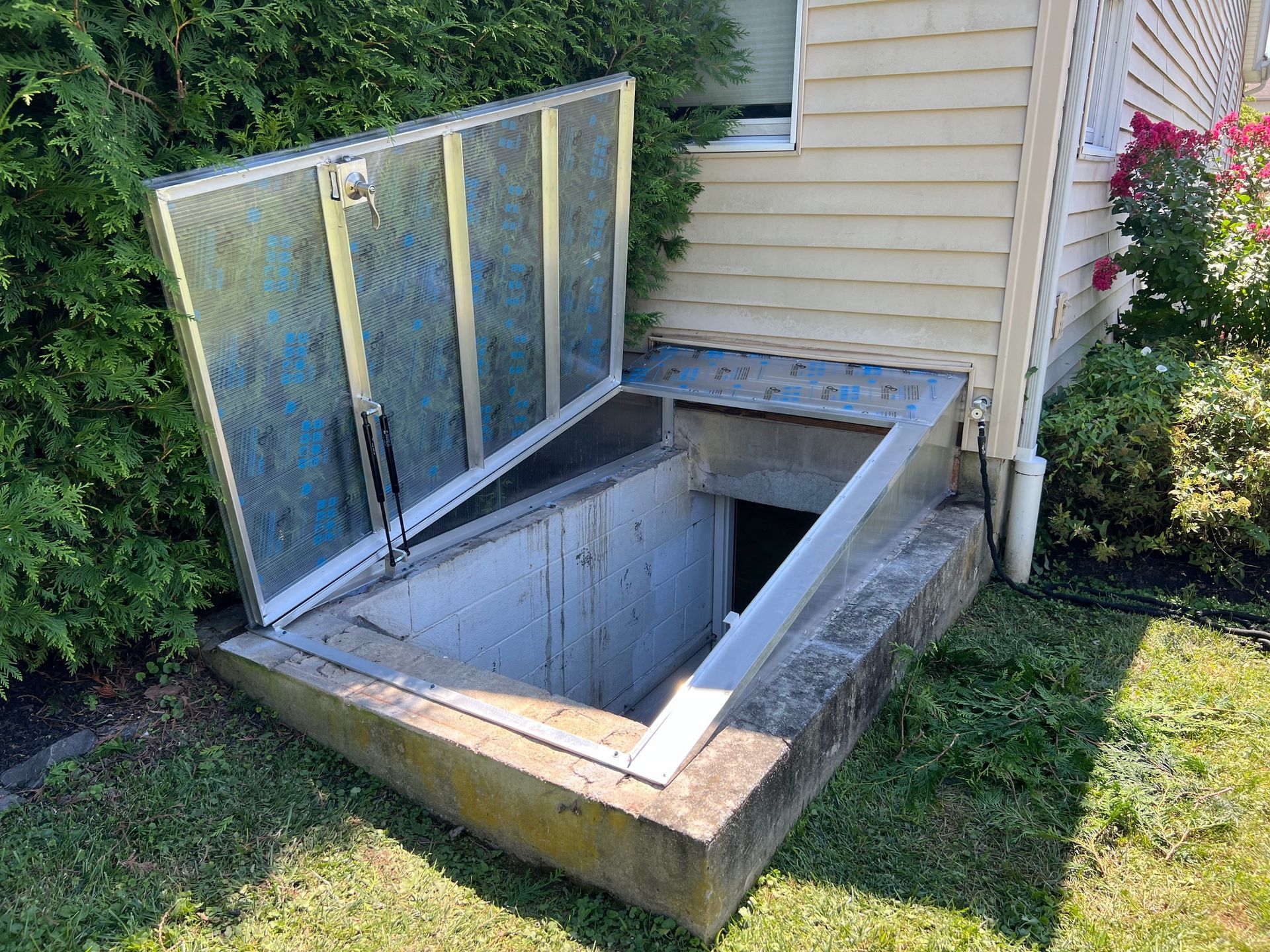 A basement door with a glass cover is sitting in the grass next to a house.