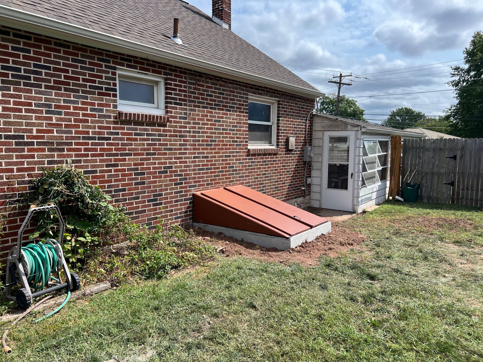 A brick house with a shed and a hose in the backyard.
