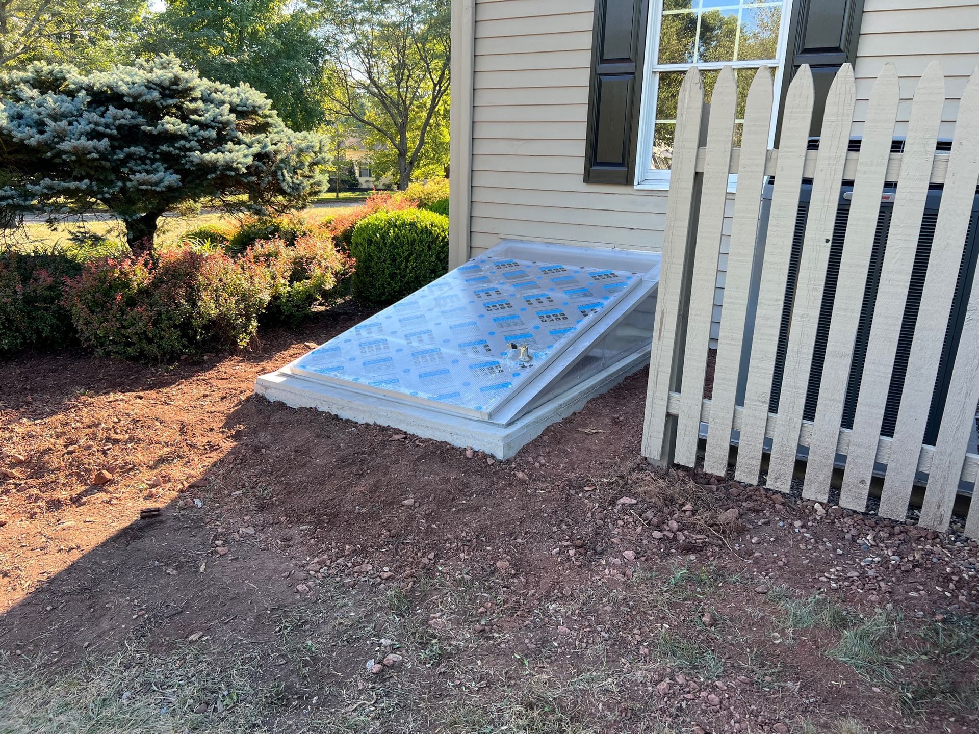 A white picket fence is sitting next to a window next to a house.