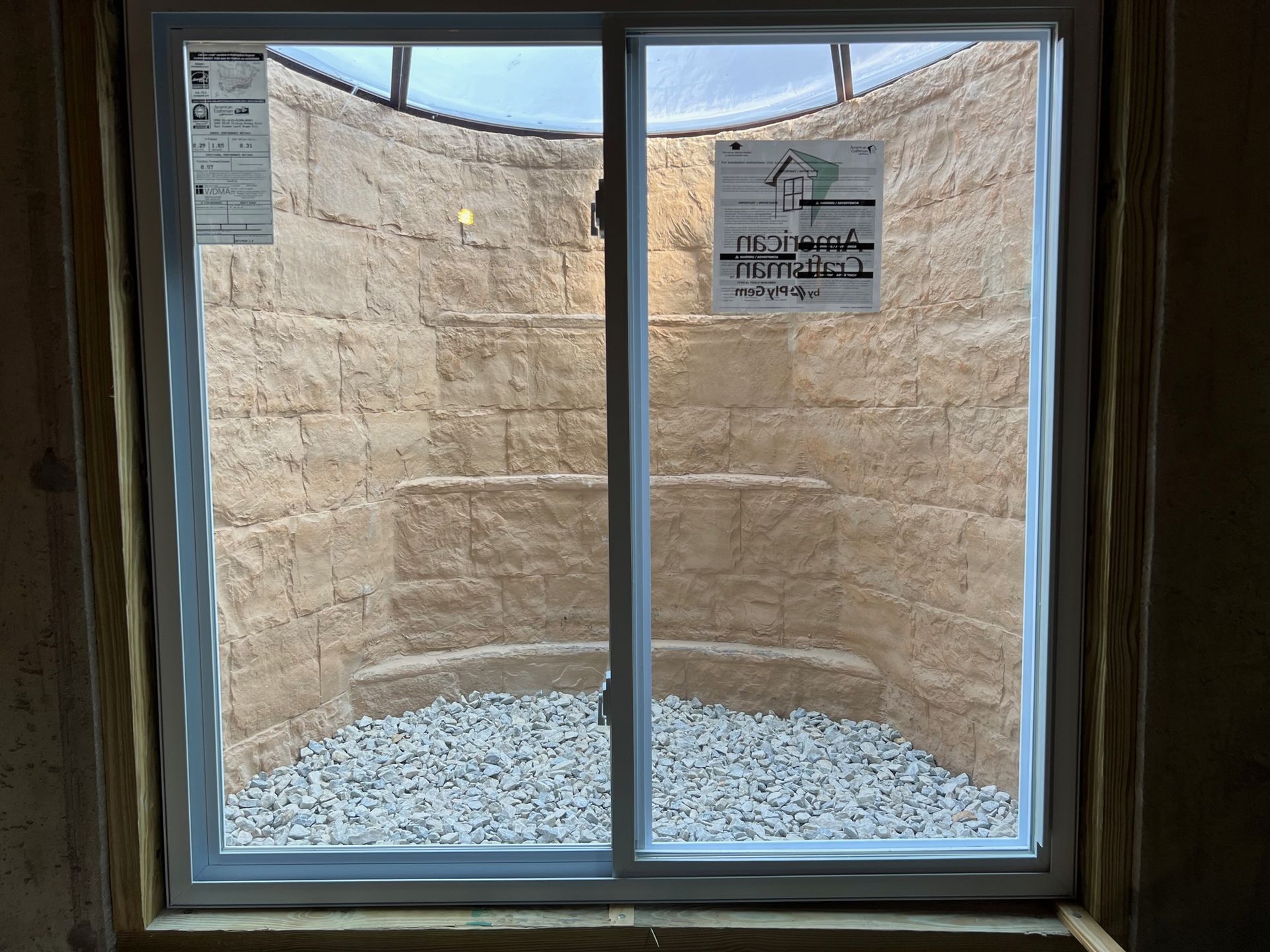 A window in a room with a brick wall and gravel in front of it.