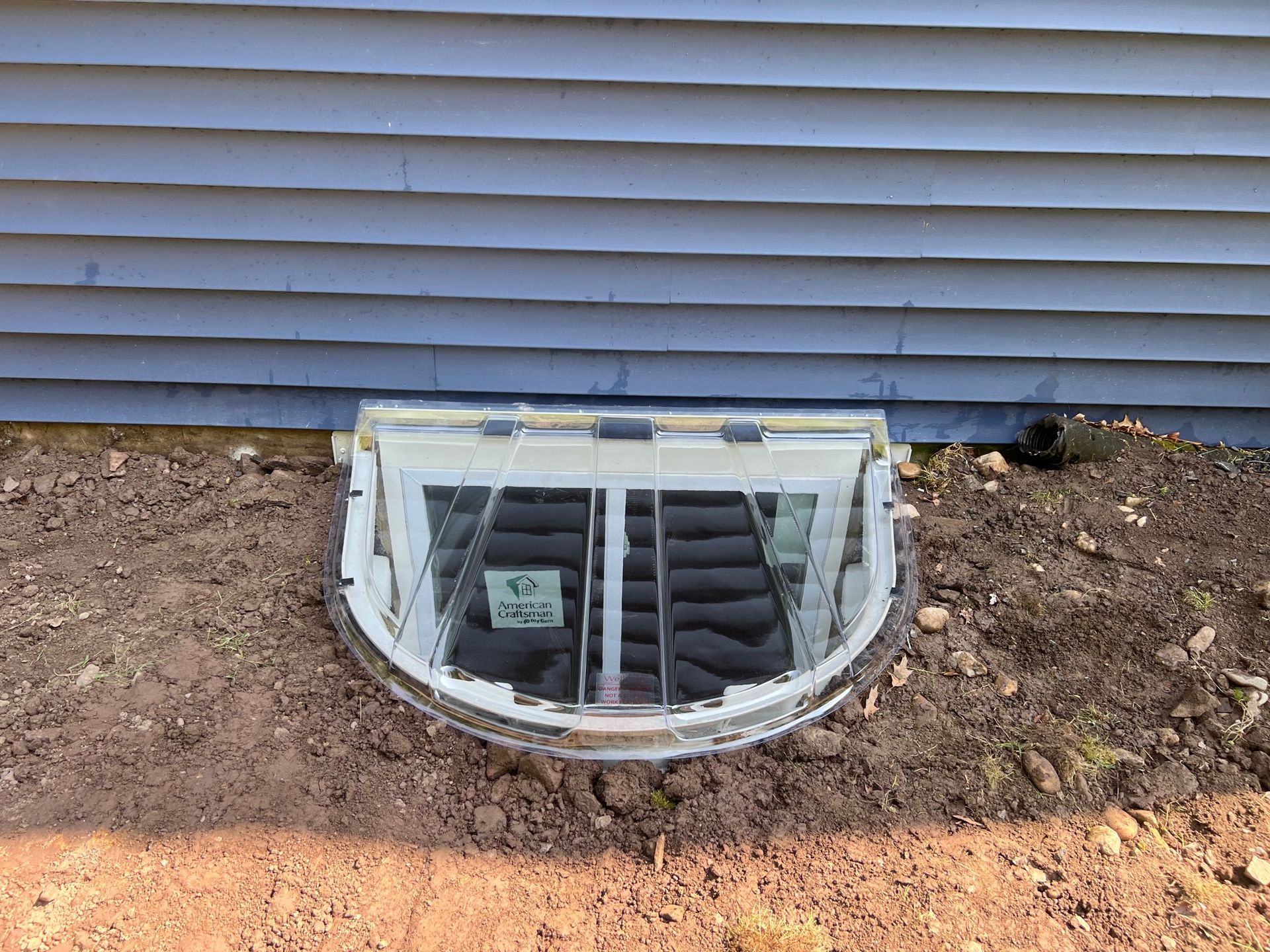 A window well in the ground next to a house.