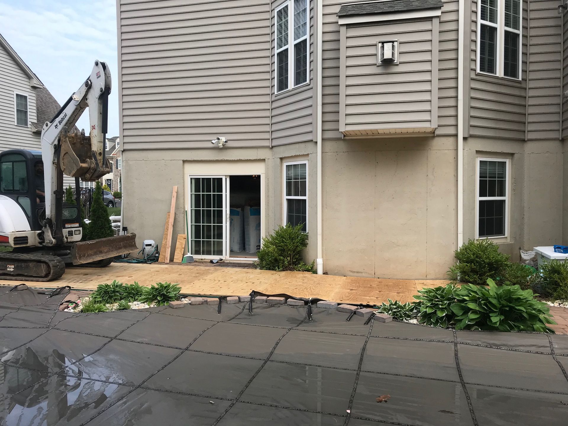 A house is being remodeled with a small excavator parked in front of it.