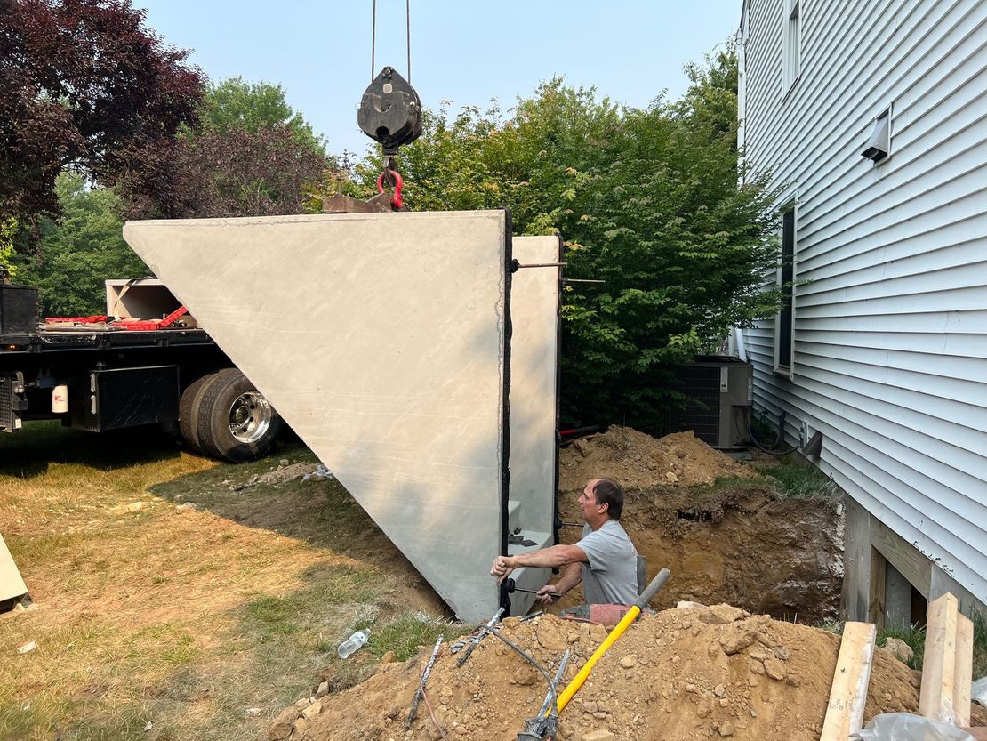 A man is sitting in the dirt next to a large piece of concrete being lifted by a crane.