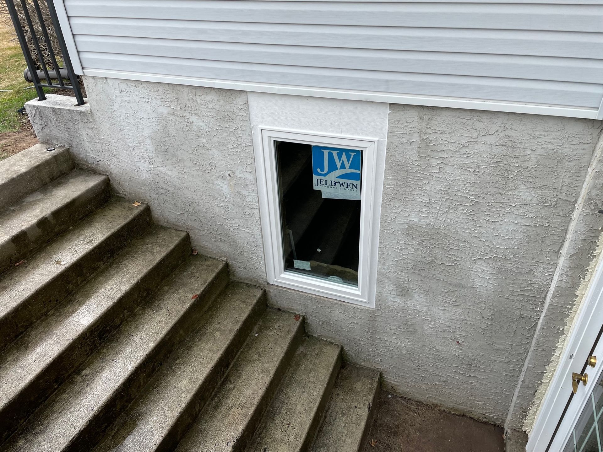Concrete stairs leading down to a basement window with a white frame, below light gray siding.