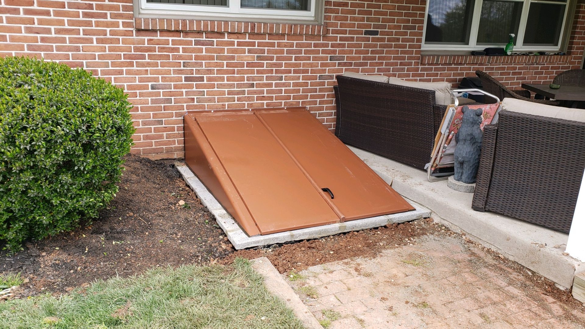 Brown cellar door entrance next to a brick building, with brown panels.