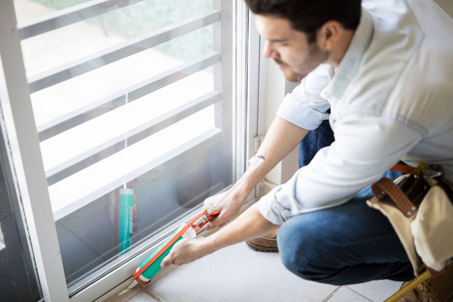 A man is kneeling down and applying sealant to a window.