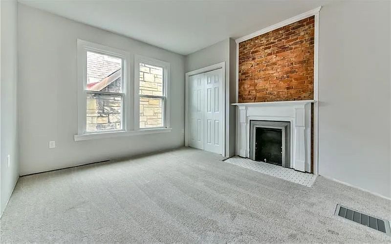 An empty living room with a fireplace and a brick wall.