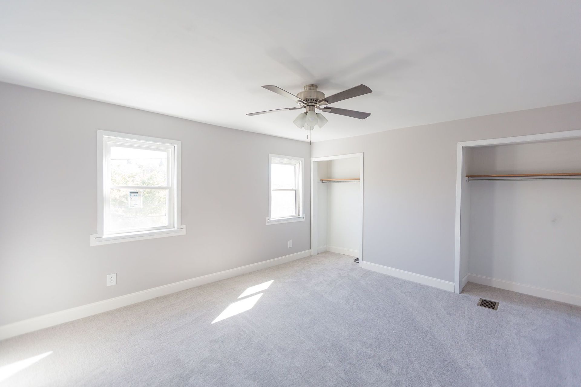 An empty bedroom with a ceiling fan and two windows.