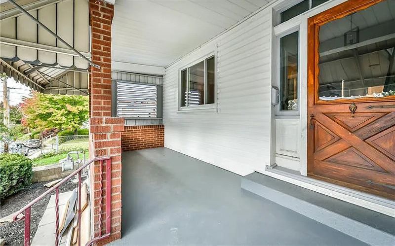 There is a porch with a wooden door and a brick wall.