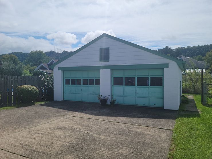 A white and green garage with a driveway in front of it.
