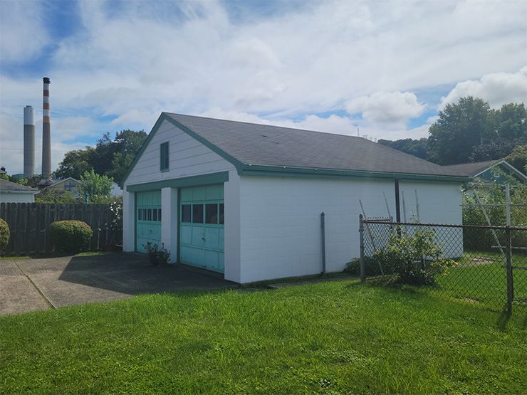 A white garage with a green door is in the backyard of a house.