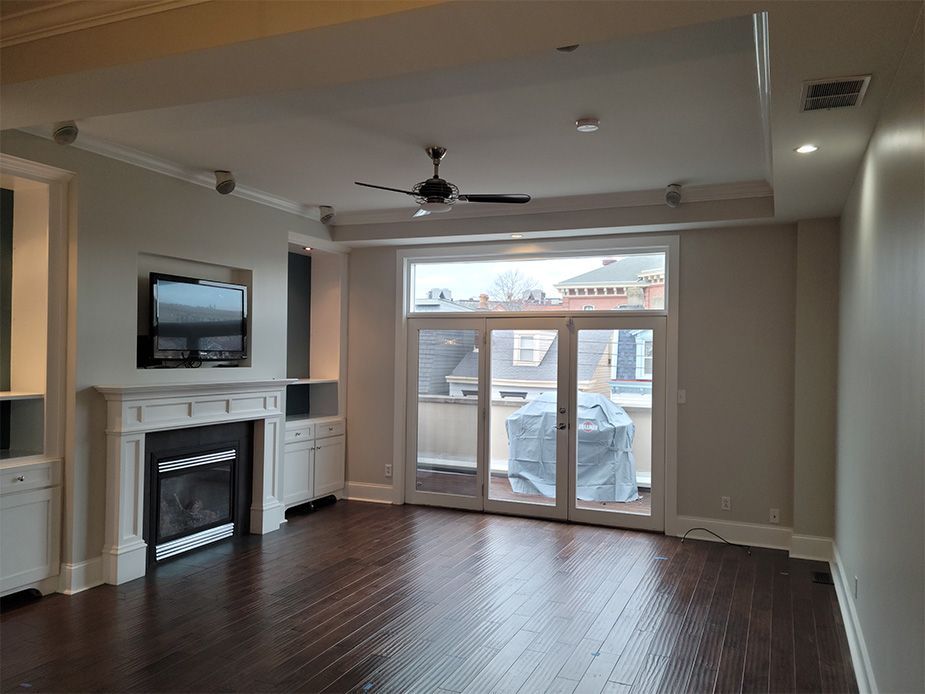 An empty living room with hardwood floors , a fireplace , a television and a ceiling fan.