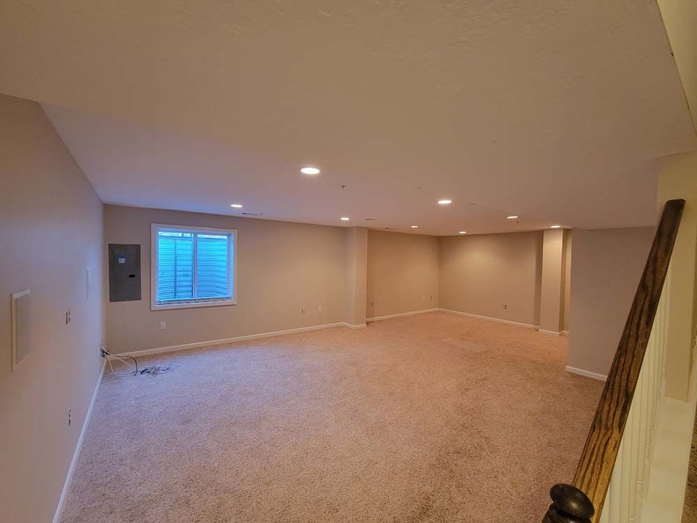 An empty basement with a staircase and a window.