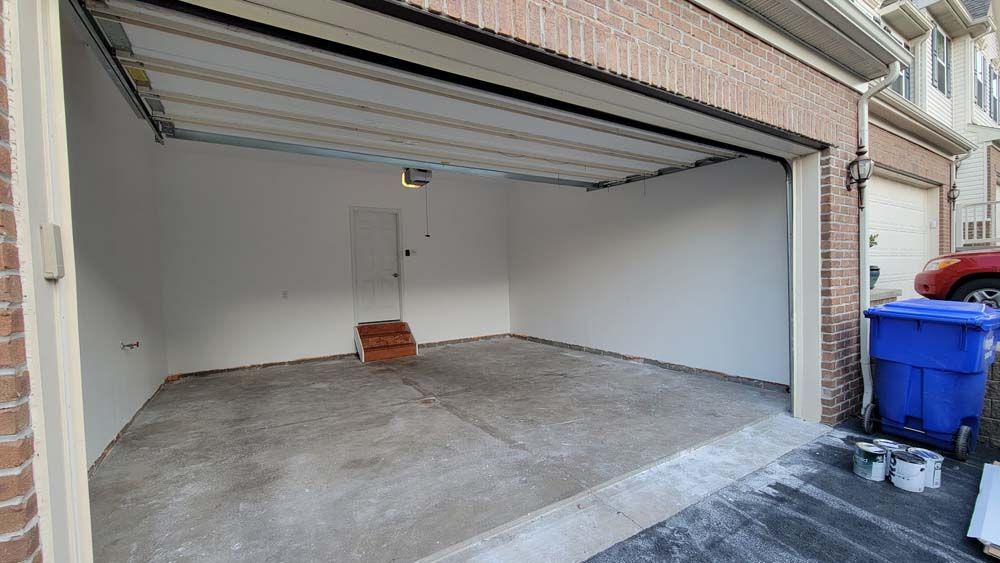 An empty garage with a blue trash can in front of it.