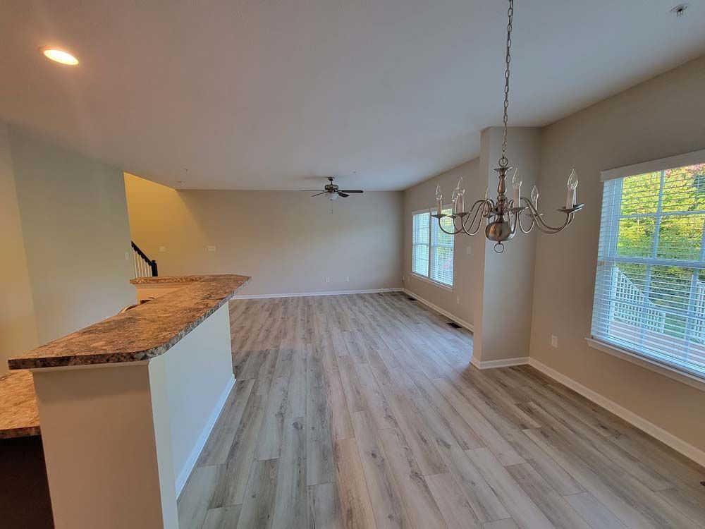 An empty living room with hardwood floors and a chandelier hanging from the ceiling.