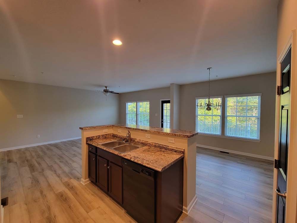 A kitchen with granite counter tops , a sink , and a dishwasher in an empty house.